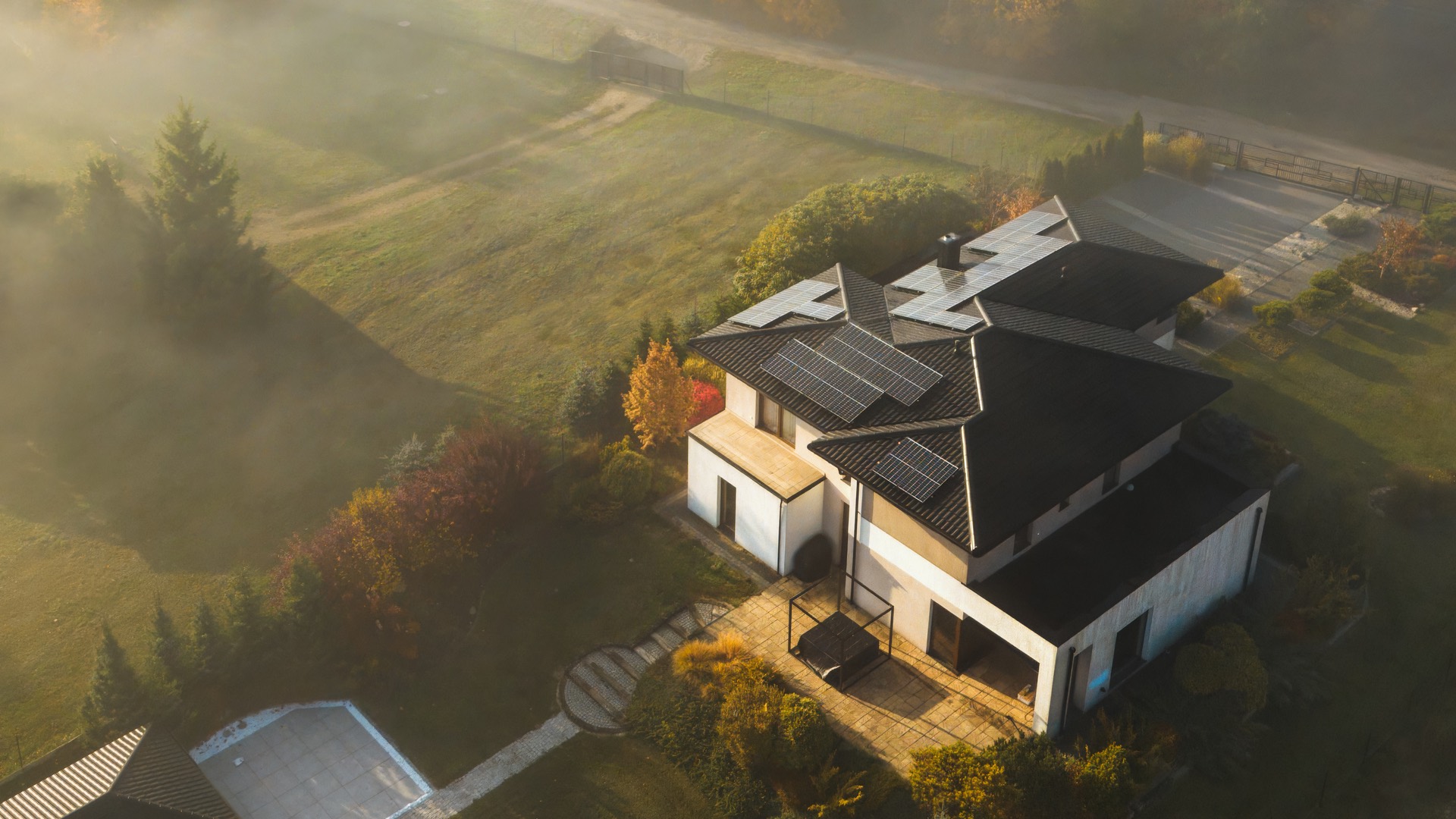 Veduta dall'alto di una casa isolata in campagna con impianto fotovoltaico, nella nebbia del mattino